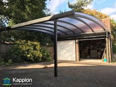 a garage with an attached carport in the middle of a brick driveway and lots of trees