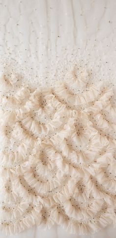 a white pillow that is on top of a bed with ruffles and beads