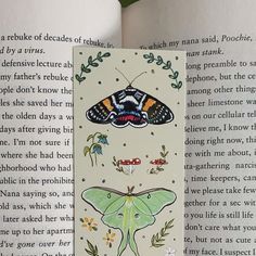 a bookmark with an image of a butterfly and moths on it, in front of a page from a book