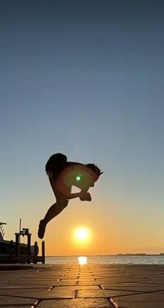 a person jumping up into the air on a skateboard near the ocean at sunset