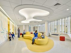 a group of people sitting on yellow couches in a large room with lots of windows