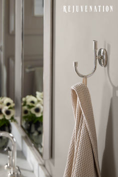 a towel hanging on a hook in front of a bathroom mirror with flowers behind it