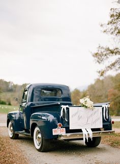 an old blue truck with a sign on it's back sitting in the road