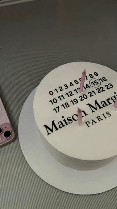 a white cake with pink butterflies on it sitting next to a cell phone and remote control