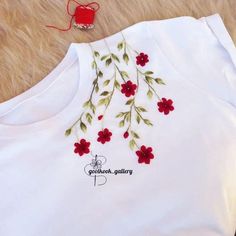 a white t - shirt with red flowers and green leaves embroidered on the chestline