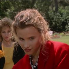 two young women are sitting on the grass and one is wearing a red jacket, while the other wears a yellow shirt