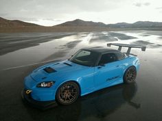 a blue sports car is parked on the wet pavement by the water's edge