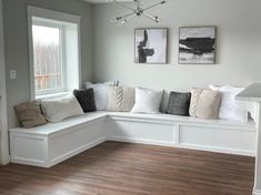 a room with white walls and wooden floors has several pillows on the windowsills