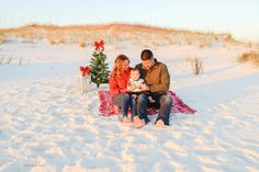 a man and woman are sitting in the snow with a small child next to a christmas tree