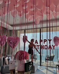 a woman standing in front of a window with pink balloons hanging from it's ceiling