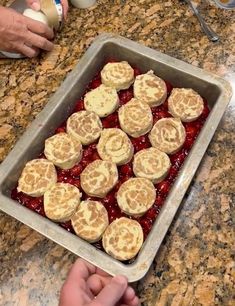 a pan filled with food sitting on top of a counter next to a person's hand