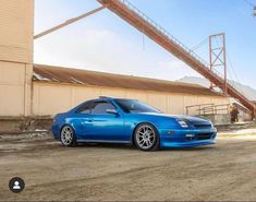 a blue sports car parked in front of a building with a large metal structure behind it