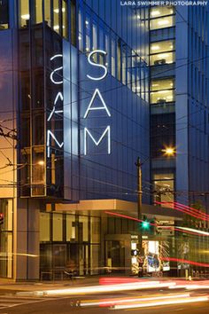 an illuminated sign on the side of a tall building at night with cars passing by