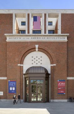 people walking in front of the museum of the american revolution, which is located on an old brick building