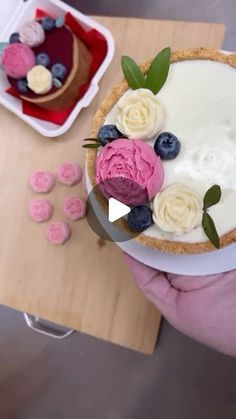 a person is holding a pie with flowers on it and blueberries in the background