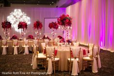 the tables are set up with white linens and red flower centerpieces on them