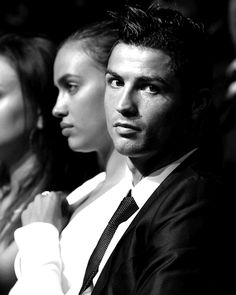 two people sitting next to each other in front of a crowd, one man wearing a suit and the other woman with her hand on her chest