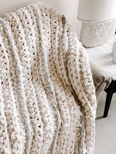 a white crocheted blanket sitting on top of a wooden chair next to a lamp