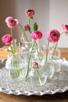 small vases with pink flowers in them on a glass platter, ready to be used as flower arrangements