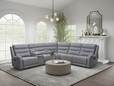 a living room with a sectional couch and round coffee table in front of two windows