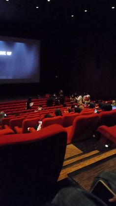 people sitting in red chairs watching a movie on the screen at an auditorium or theater