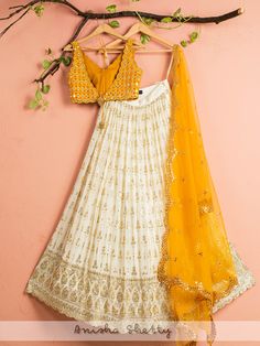 A three-piece ivory and yellow mirror lehenga set from the Anisha Shetty collection. This gorgeous ivory georgette lehenga is paired with a yellow mirror blouse in raw silk fabric. The ivory lehenga is enhanced with heavy sequence work all over with scalloped edging. The V neck mirror blouse has scalloped edging all over with a ghungroo tassel tie-up at the back.  This outfit is completed with a yellow net dupatta with heavy embroidery scalloped edging. White Kundan Lehenga With Cutdana, White Georgette Dresses With Gota Work, Yellow Chinon Anarkali Set With Cutdana, Yellow Cutdana Chinon Dress, Yellow Lehenga With Zari Work In Chinon, Yellow Dola Silk Lehenga With Gota Work, Cream Georgette Lehenga For Festivals, Yellow Traditional Wear With Mirror Work For Reception, Yellow Dola Silk Lehenga With Mirror Work