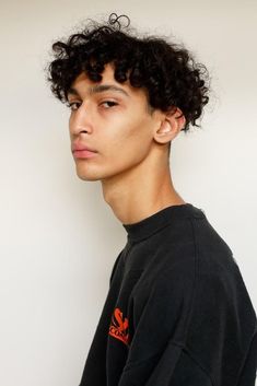 a young man with curly hair wearing a black sweatshirt and looking off to the side