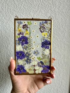 a hand holding up a small glass frame with flowers on it