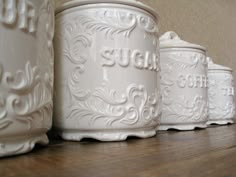 three white canisters sitting on top of a wooden table