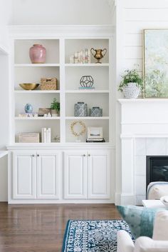 a living room with white bookcases and blue rug in front of the fireplace