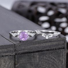 an engagement ring and wedding band set with a pink stone in the center, sitting on top of a wooden box