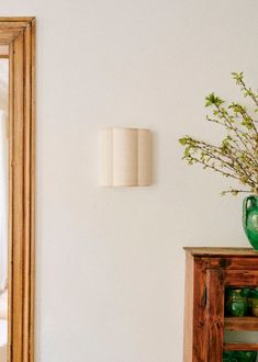 a green vase sitting on top of a wooden table next to a mirror and shelf