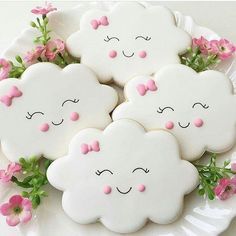 four decorated cookies sitting on top of a white plate with pink flowers in the background