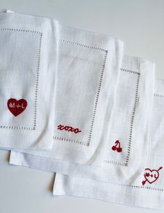 four white napkins with red embroidered designs on them