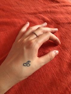 a woman's hand with a small tattoo on her left wrist, resting on a red blanket