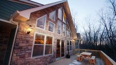 a wooden deck with two benches next to a stone and wood house at dusk time