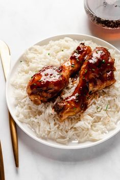 two pieces of chicken with sauce on top of rice in a white bowl next to gold utensils