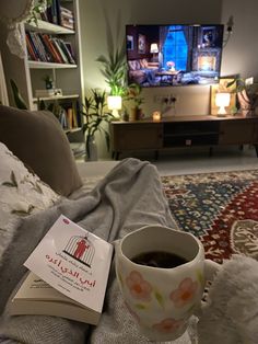 a cup of coffee sitting on top of a bed next to a book