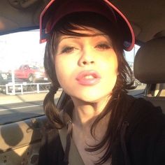 a woman wearing a baseball cap sitting in the back seat of a car with her tongue out