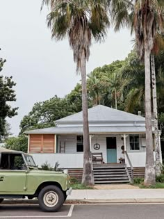 a green truck is parked in front of a white house with palm trees around it