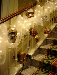 several masks are hanging on the banisters in front of stairs decorated with lights