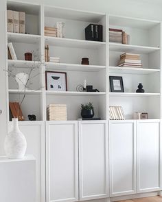 a white bookcase filled with books next to a vase on top of a wooden floor