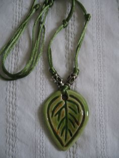 a green necklace with a leaf shaped pendant hanging from it's side on a white cloth