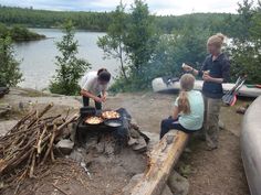 three people cooking food over an open fire