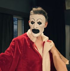 a man in a red robe with a white face and black nose painted on it