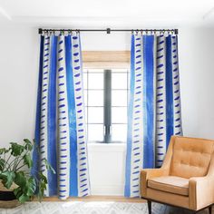 a living room with blue curtains and a chair in front of a window that has a potted plant next to it