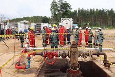 some people in red suits and yellow ties are standing around an open pit with pipes