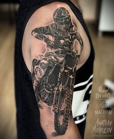 a man with a black and grey tattoo on his arm is riding a dirt bike