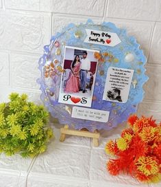 a couple's photo frame with flowers in front of it and a vase on the side