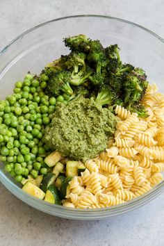 a bowl filled with pasta, peas and broccoli on top of a table